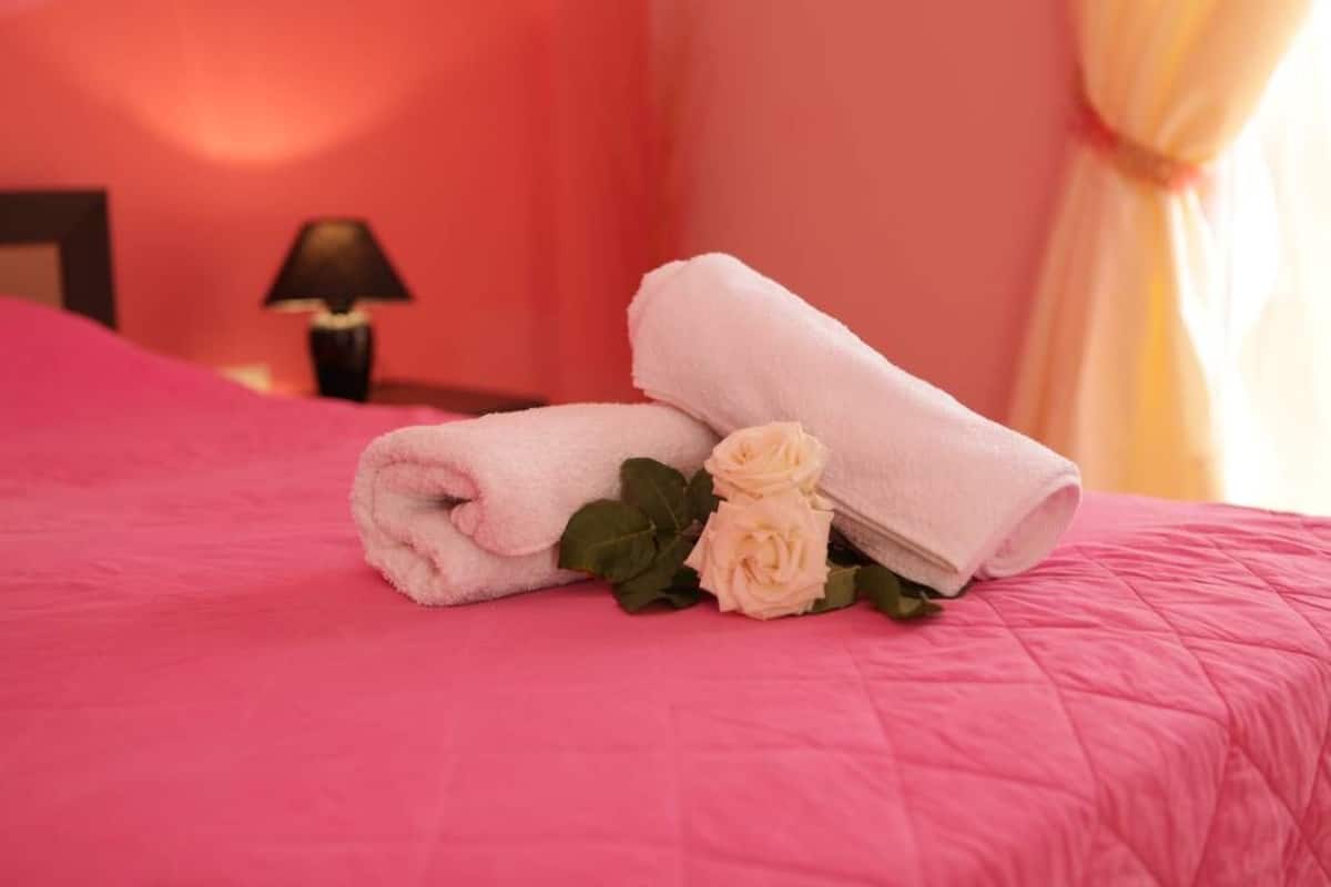 A bed with pink bedding, a rolled white towel, and two white roses.