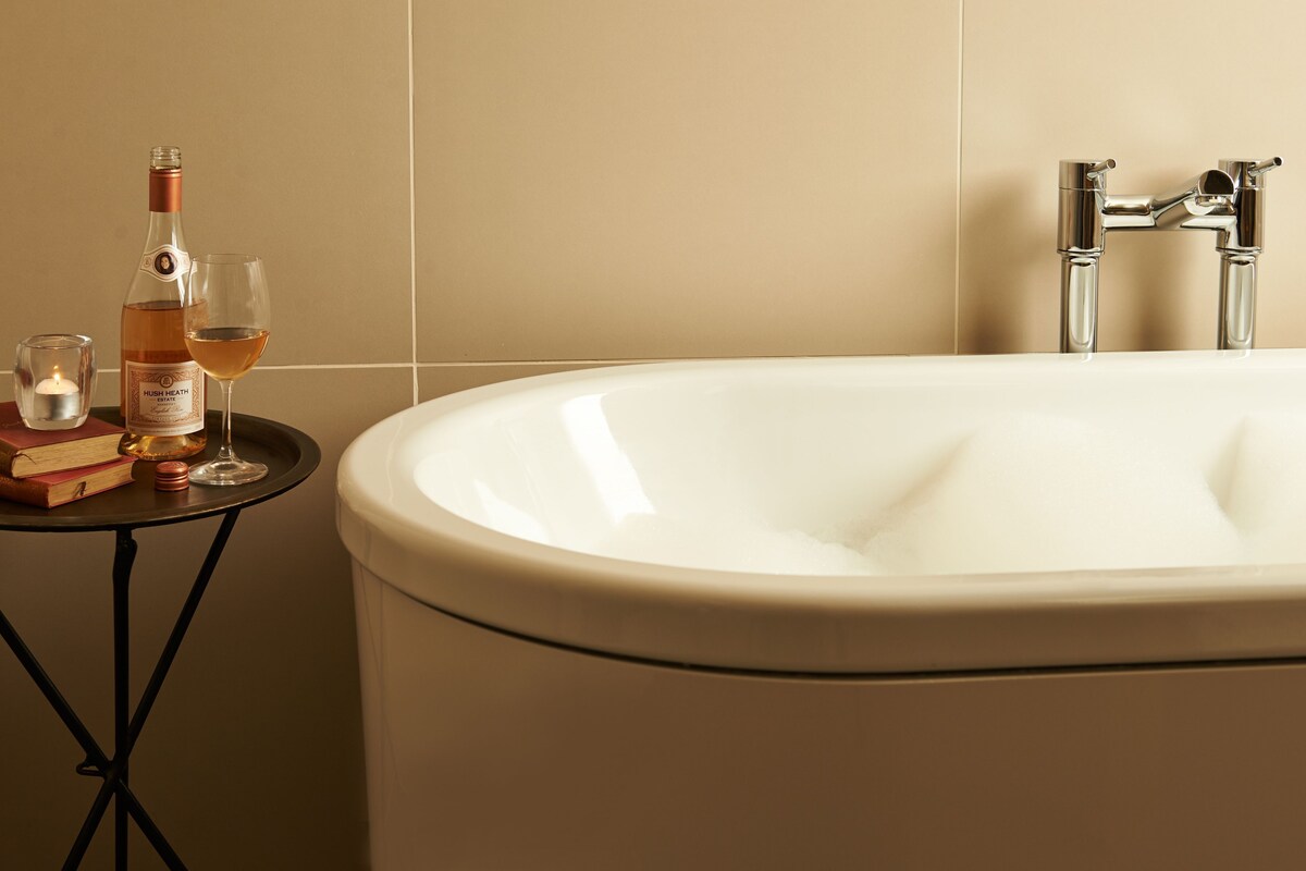 Une salle de bain avec une baignoire, un lavabo, un miroir et une table sur laquelle se trouvent une bouteille et un verre.
