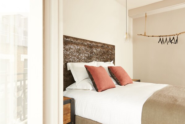 A neatly made bed with white and brown bedding, a textured headboard, and a hanging light fixture.