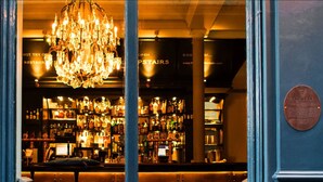 A bar with a chandelier, shelves of liquor bottles, and a plaque on the wall. - The Bull and The Hide (London)