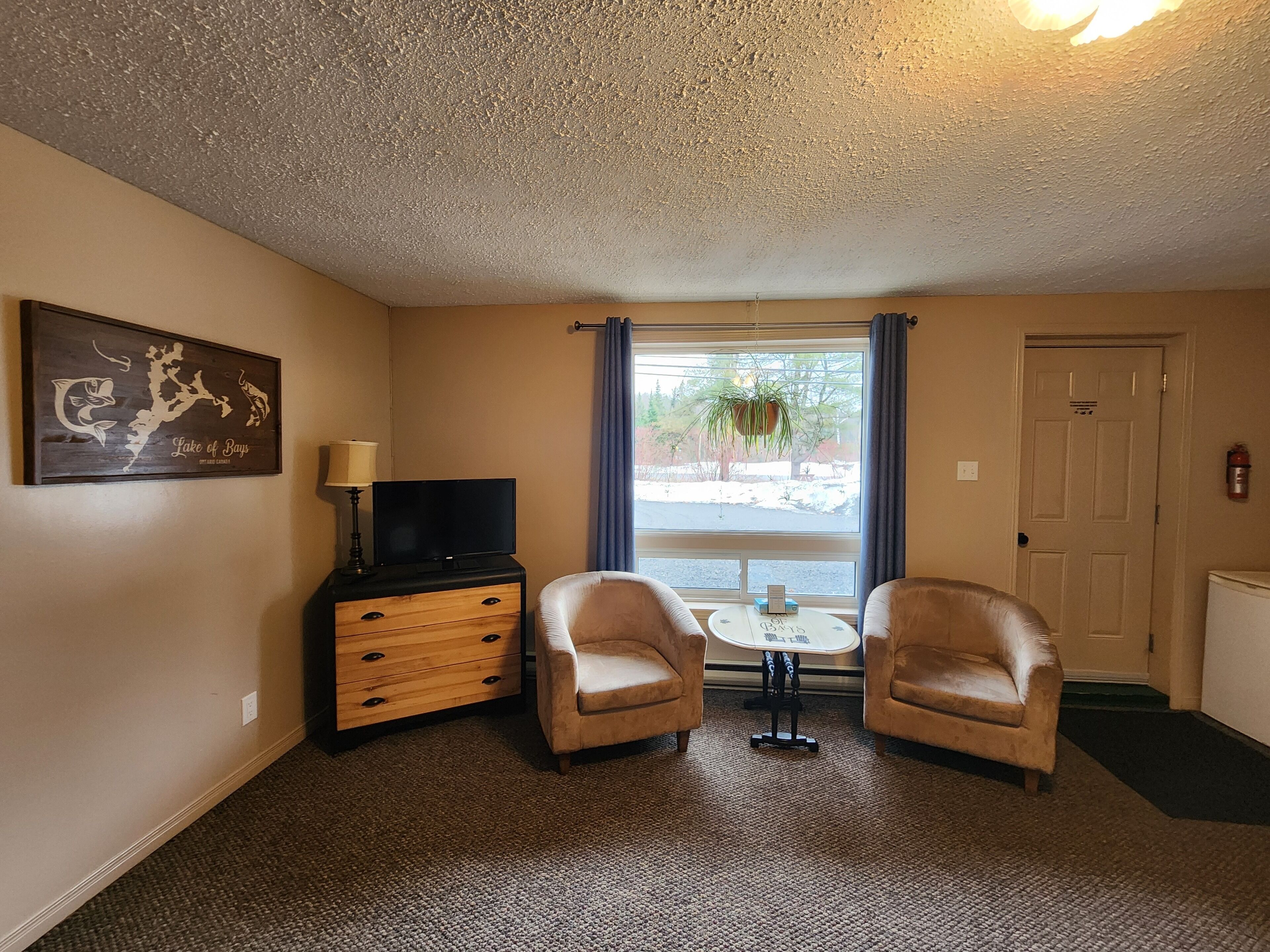 A room with two leather armchairs, a small table, a TV on a wooden cabinet, a window with curtains, and a door.