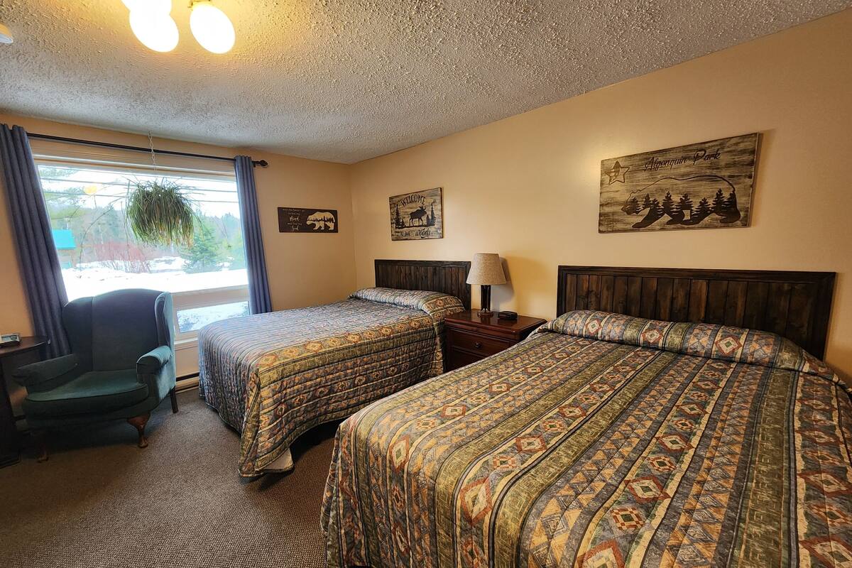Une chambre d’hôtel avec deux lits, une chaise, une table de chevet et une fenêtre avec des rideaux.