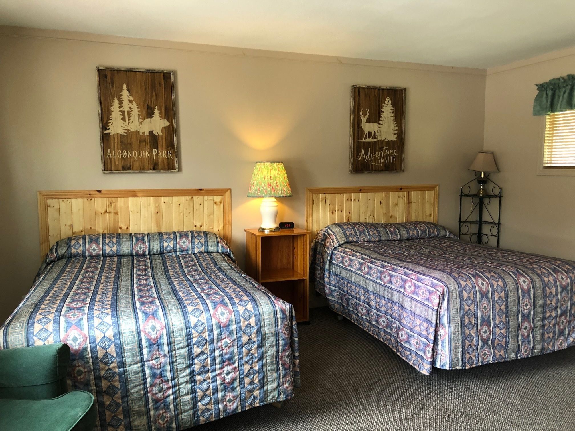 A room with two beds, a nightstand with a lamp, and two wall decorations.