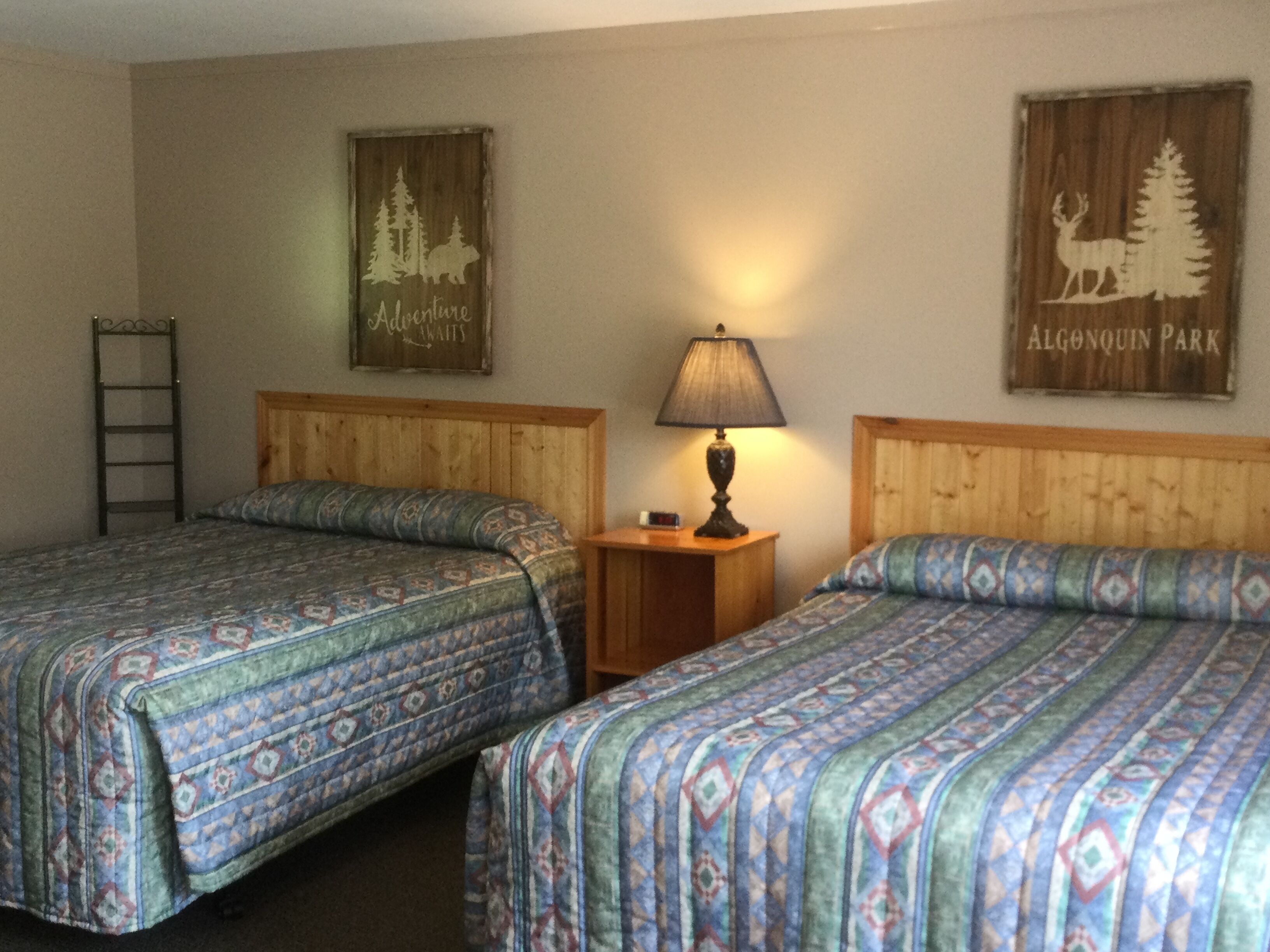 A room with two beds, a nightstand with a lamp, a ladder, and two wall decorations.