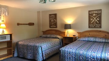 Une chambre d’hôtel avec deux lits, une tête de lit en bois, une lampe fixée au mur, un panneau décoratif encadré et une petite étagère avec une lampe.