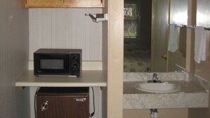 A compact bathroom with a wooden cabinet, a microwave, a sink, and a mirror. - Valley Inn (Hamilton)
