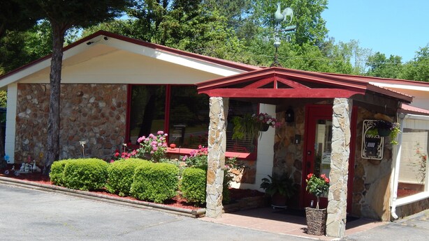 A small building with a stone facade, a red roof, and a covered entrance area with potted plants and flowers. - Valley Inn (Hamilton)