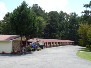 A row of motel-style buildings with a red roof, surrounded by trees.