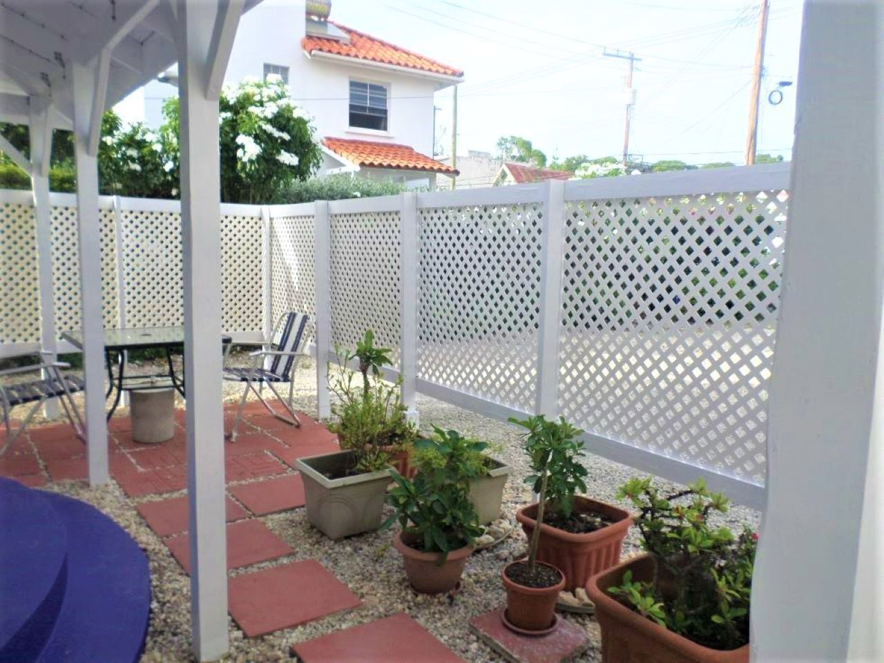 A covered patio area with potted plants, outdoor furniture, and a white lattice fence.