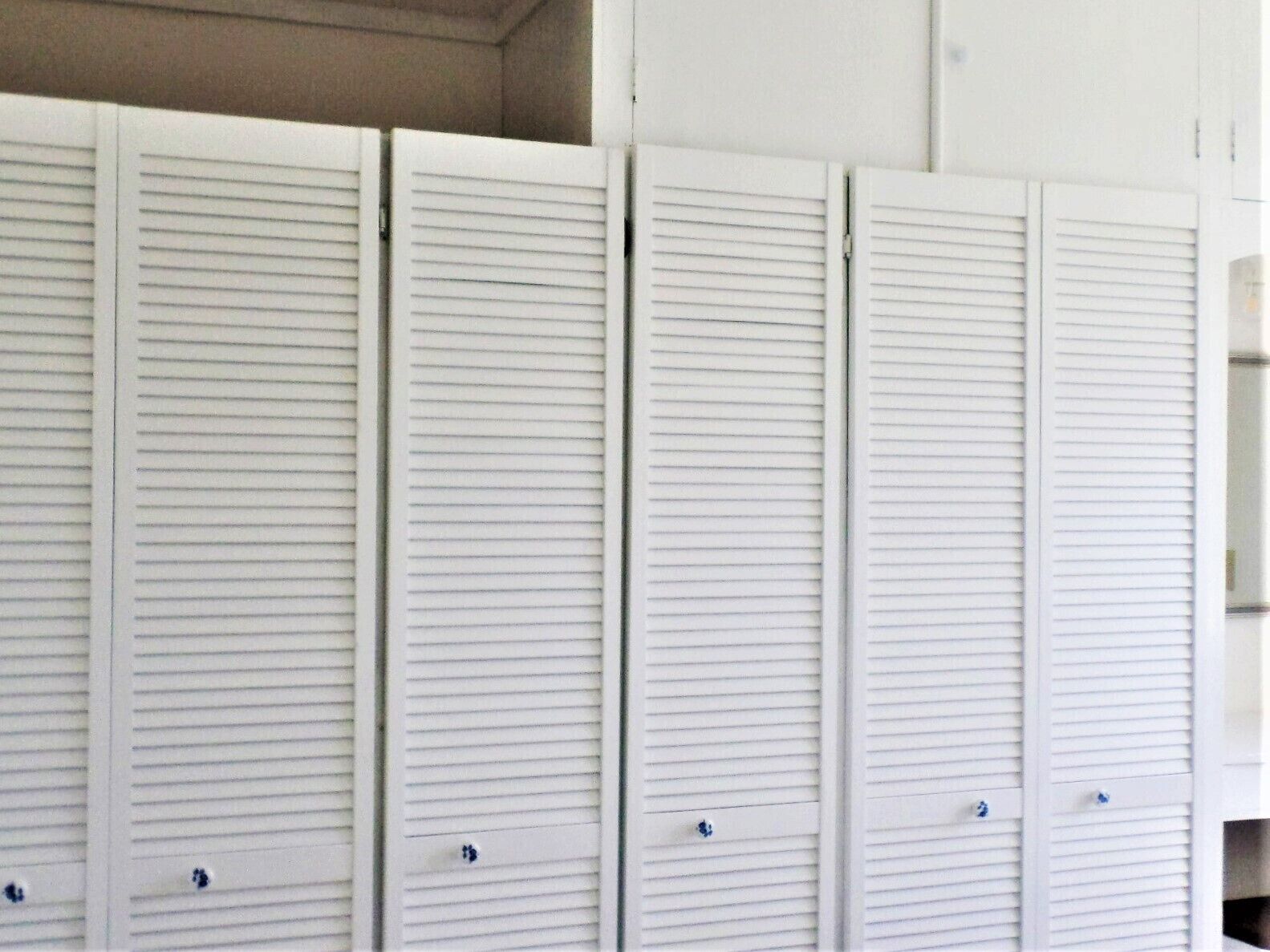 A row of white louvered closets with handles, likely in a hotel or similar accommodation.