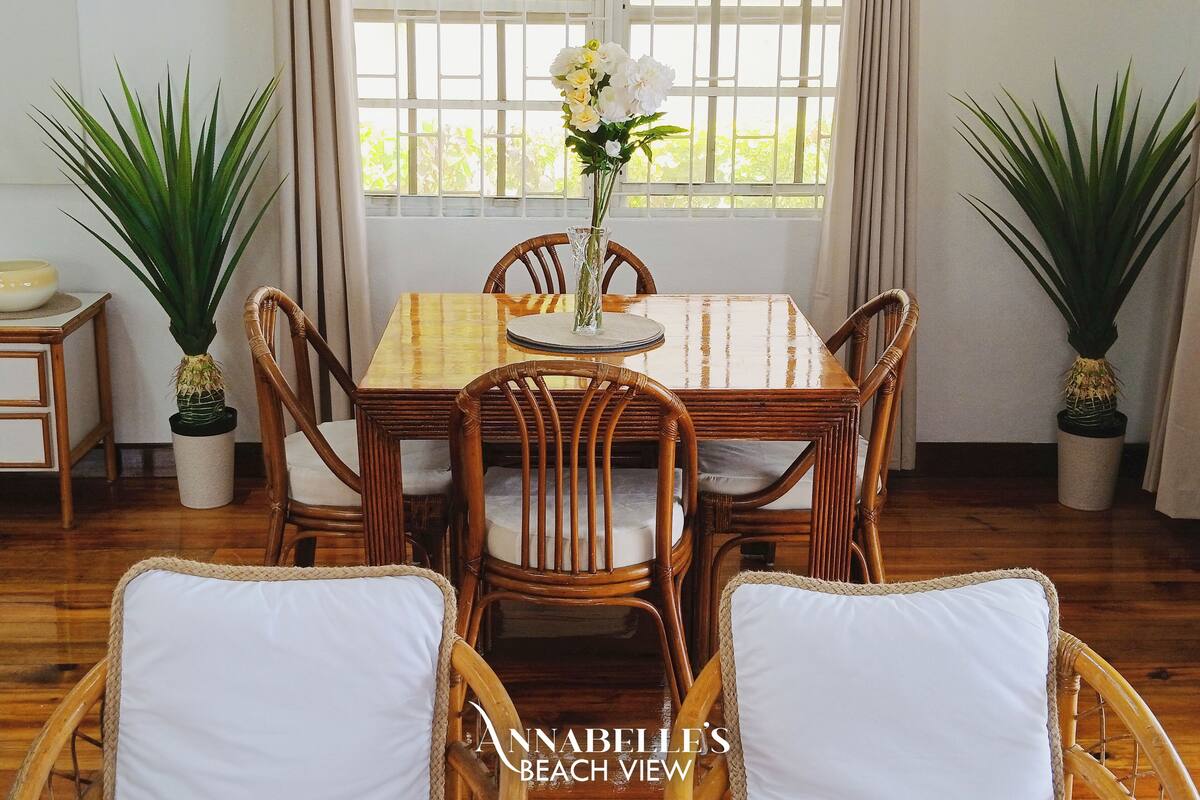 A dining area with a wooden table and chairs, a vase with flowers, and two potted plants.