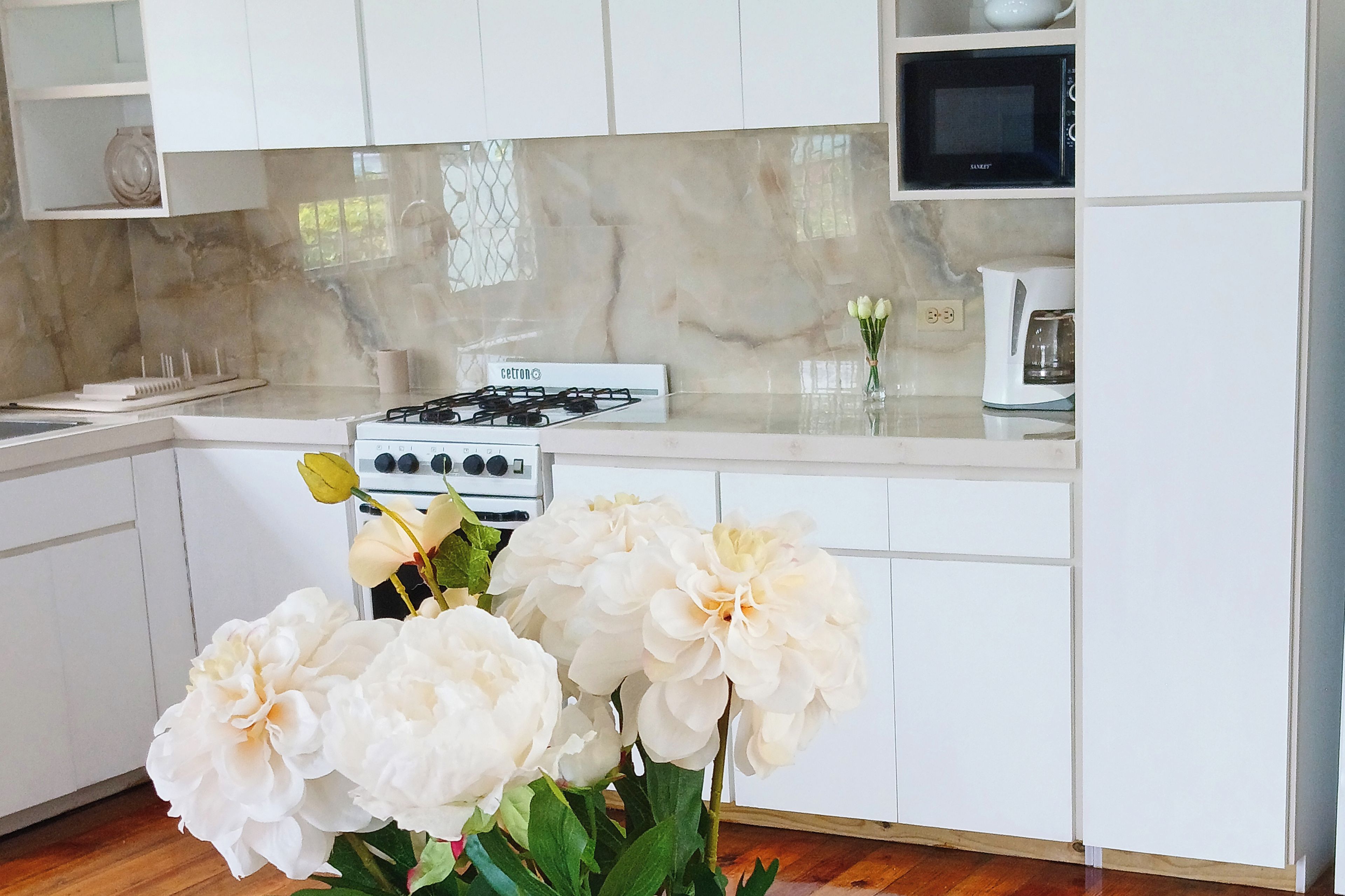 A kitchen with white cabinets, a gas stove, and a microwave. There is a vase with white flowers on the counter.