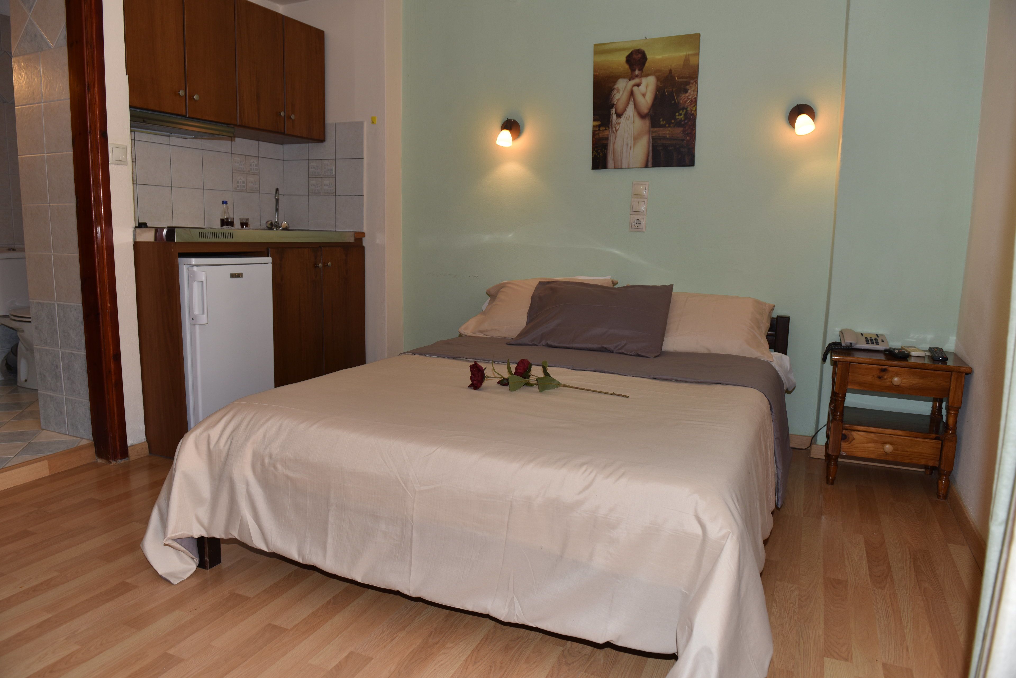 Un dormitorio con cama, mesita de noche, una pequeña mesa de madera, una lámpara de pared y un cuadro.