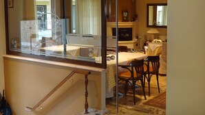 Hotelkamer met glazen scheiding, een eethoek met tafel en stoelen, een televisie en een bar.