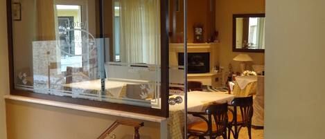 Habitación de hotel con separador de vidrio, zona de comedor con mesa y sillas, televisor y bar.