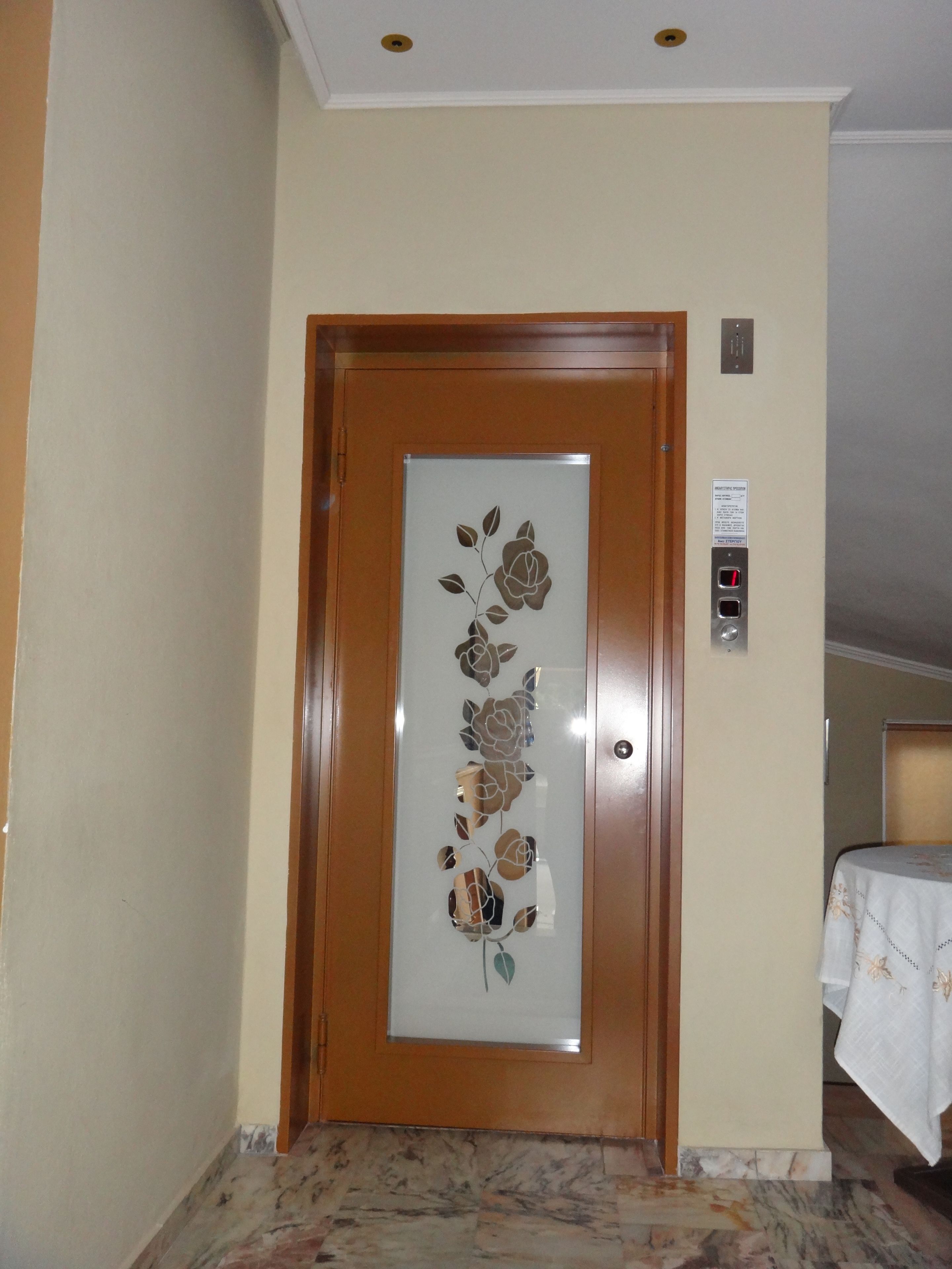 Quarto de hotel com porta de madeira decorada com motivos florais, piso de mármore e cama com colcha branca.