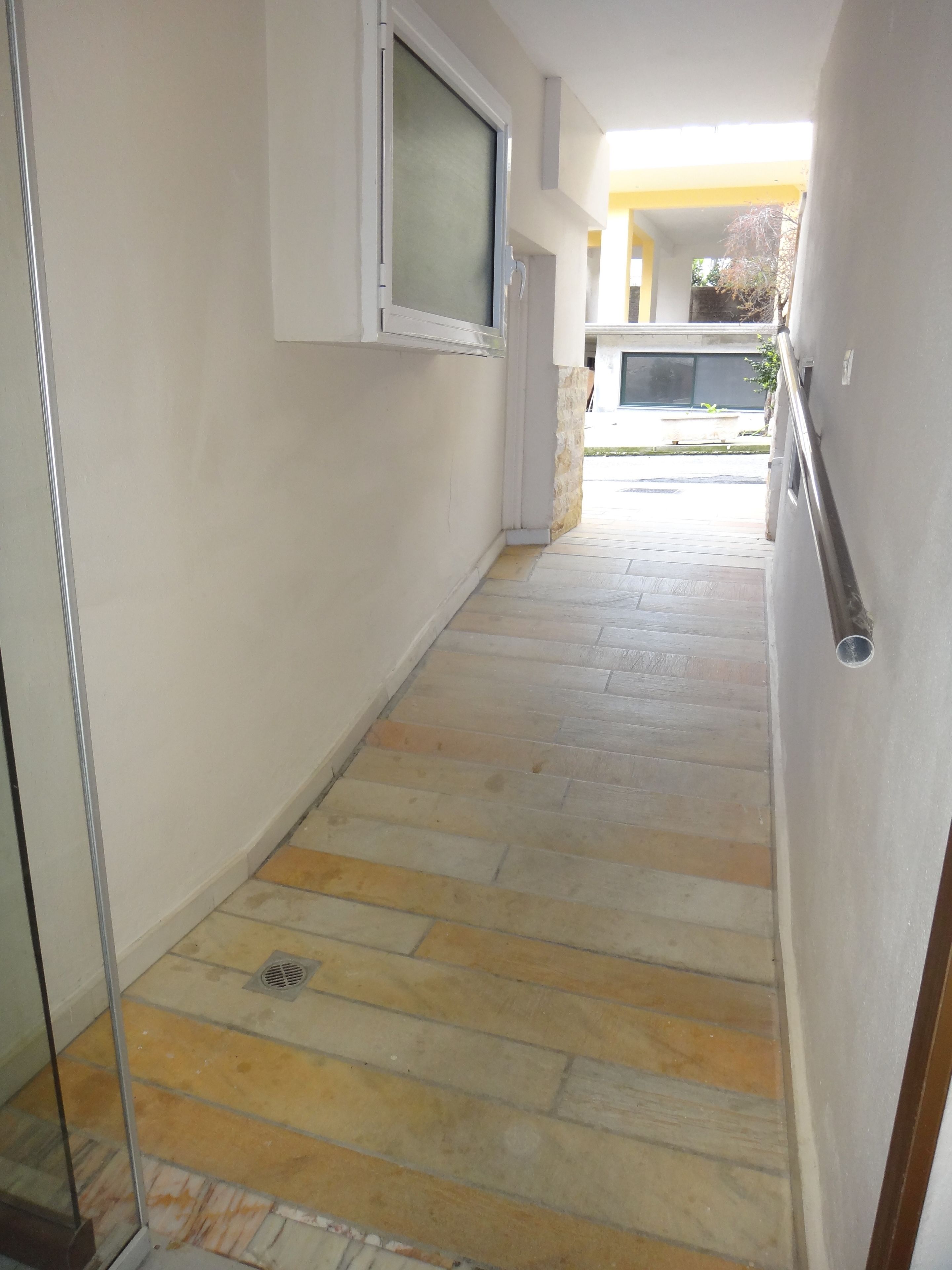 A narrow hallway with a tiled floor, a window with a screen, and a door leading to an outdoor area.