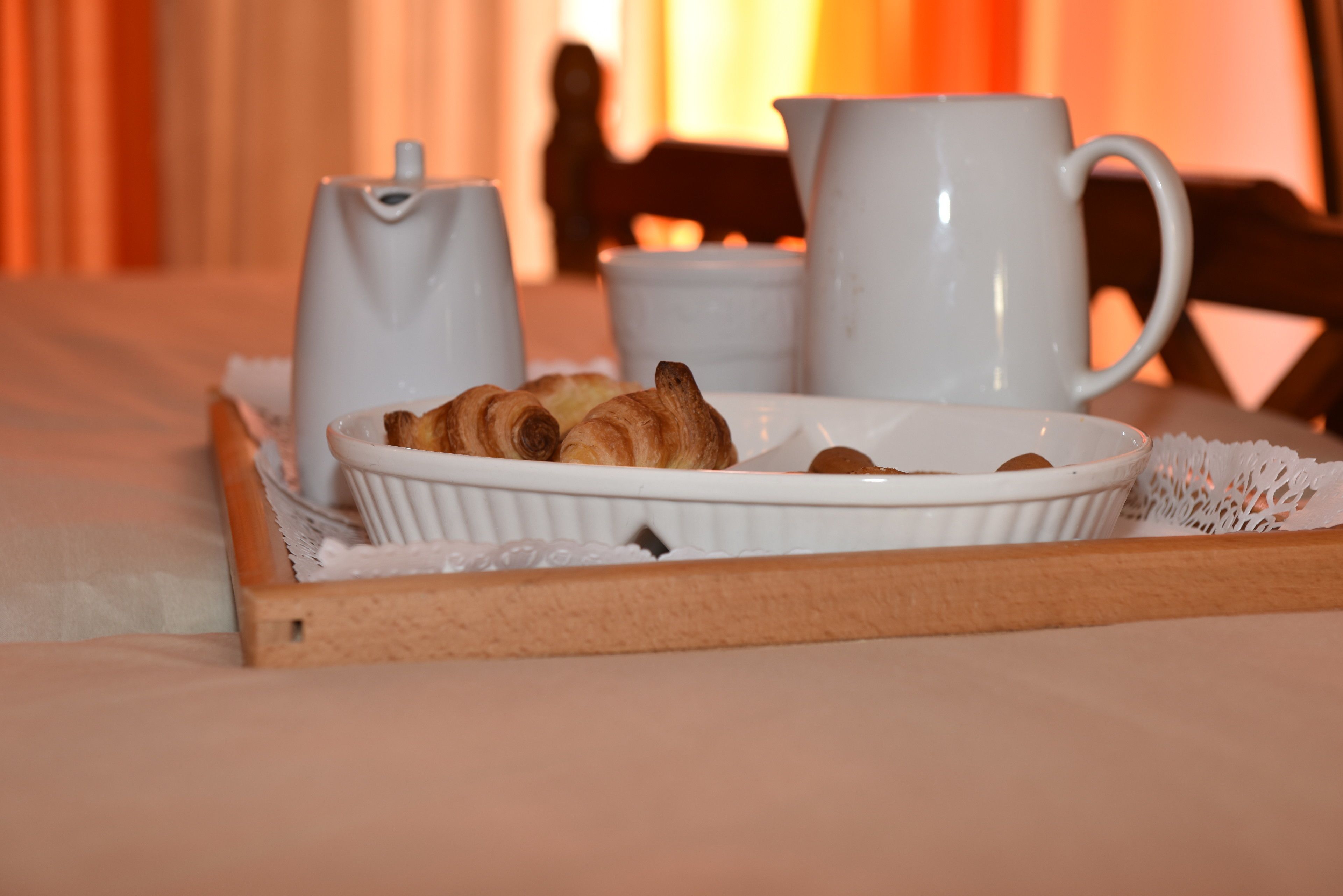 A tray with croissants and a white pitcher on a bed with a white tablecloth.