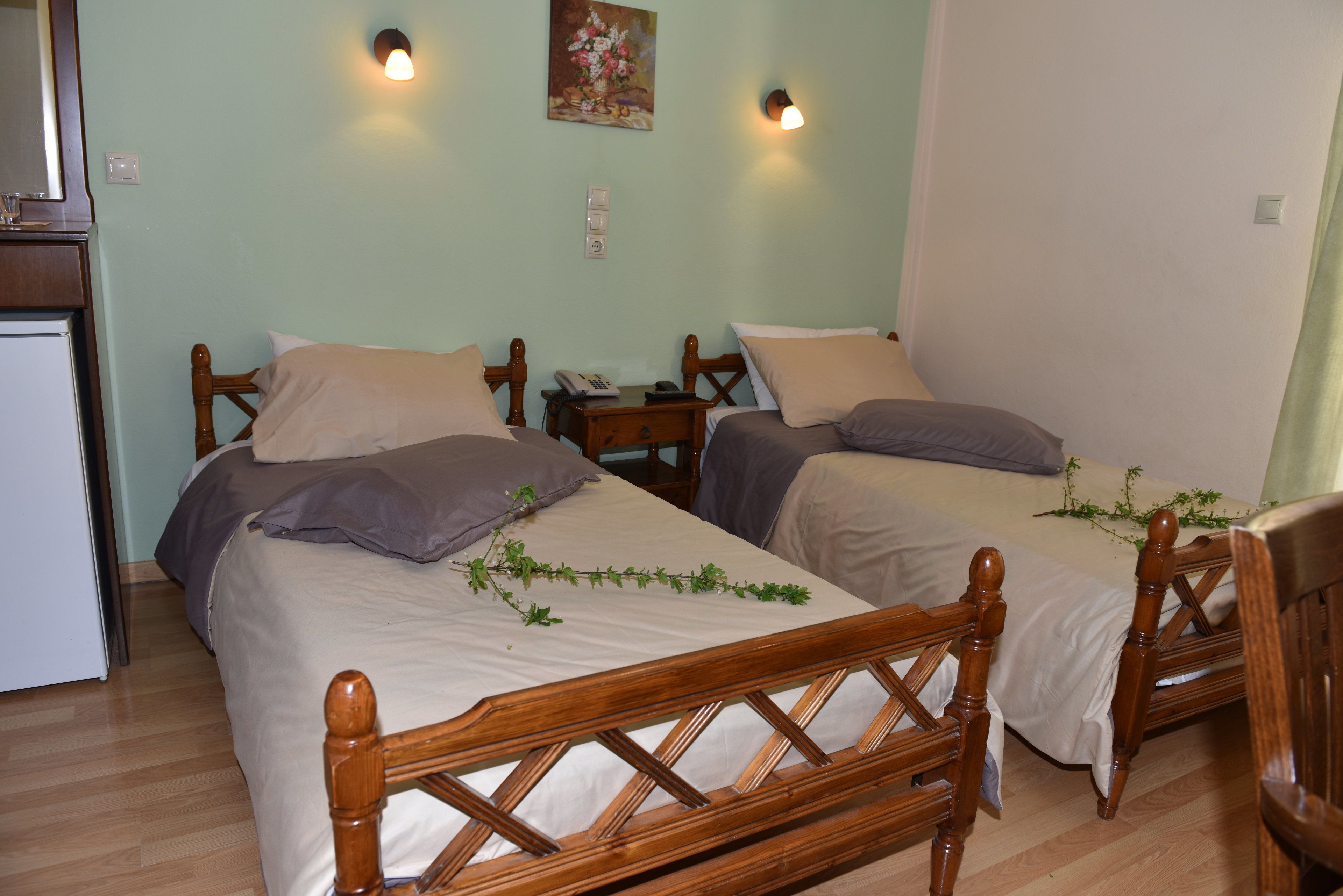 A room with two wooden beds, a small bedside table with a lamp, and a wall-mounted light fixture.