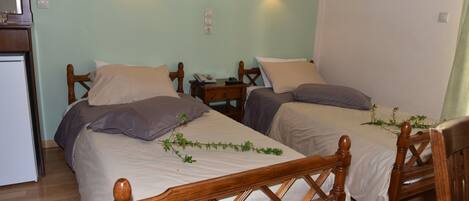 A room with two wooden beds, a small bedside table with a lamp, and a wall-mounted light fixture.