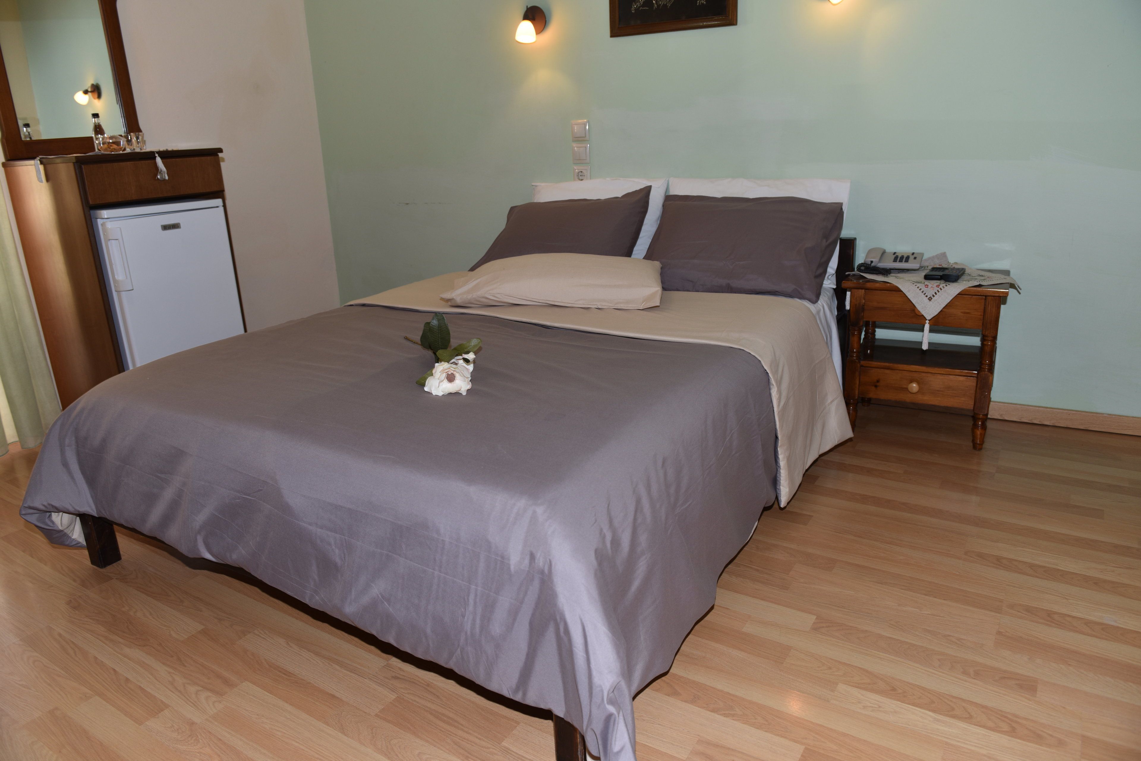A neatly made bed with a gray bedspread, a small bedside table with a lamp, and a wooden nightstand with a telephone.