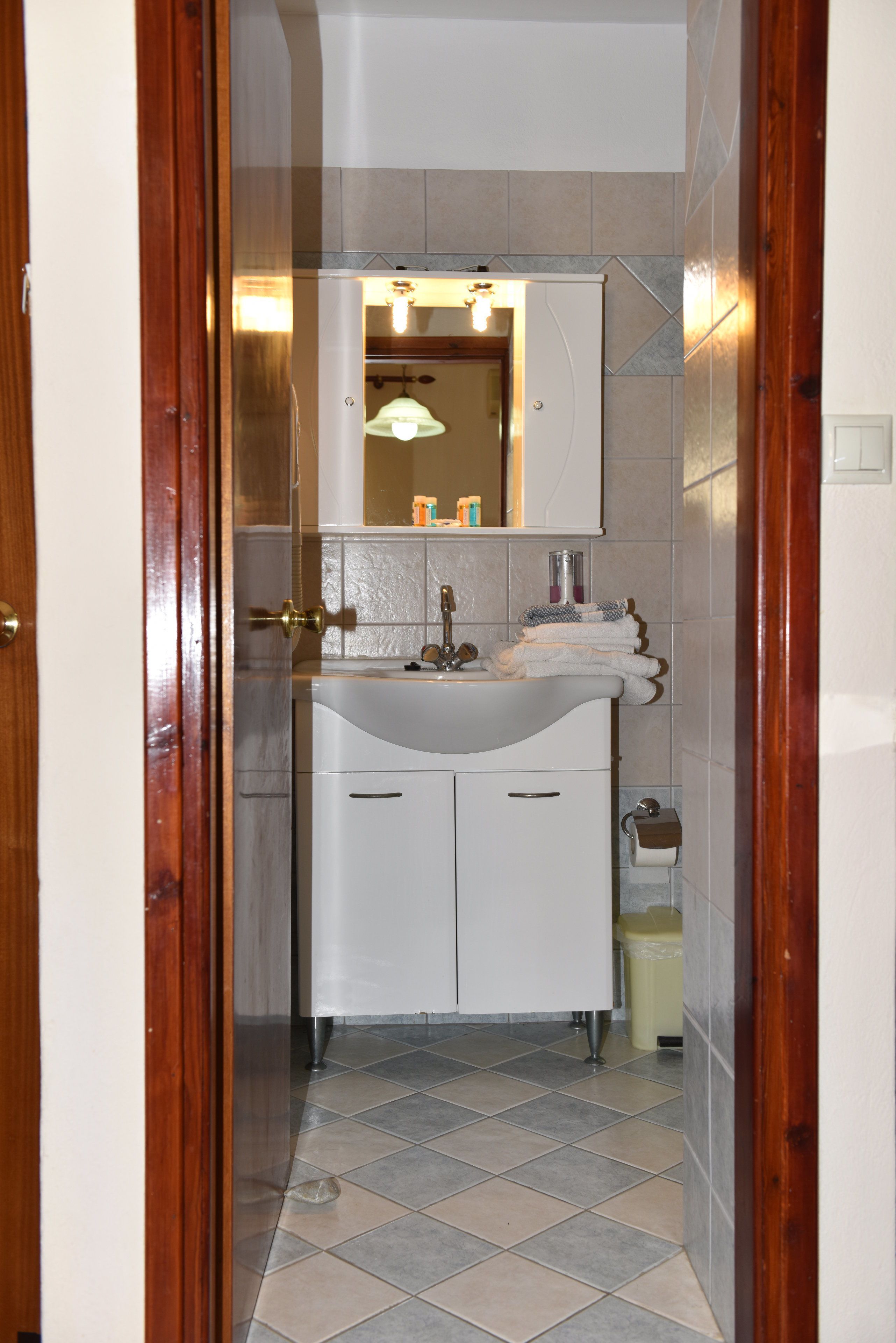 A narrow bathroom with a white sink, mirror, and tiled floor.