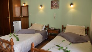 Een slaapkamer met twee bedden, houten hoofdborden, een klein nachtkastje met een lamp, een telefoon aan de muur en een houten kledingkast.