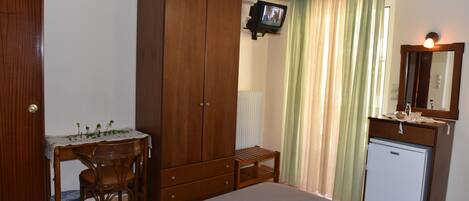 A bedroom with a bed, wooden wardrobe, desk with chair, and a small refrigerator.