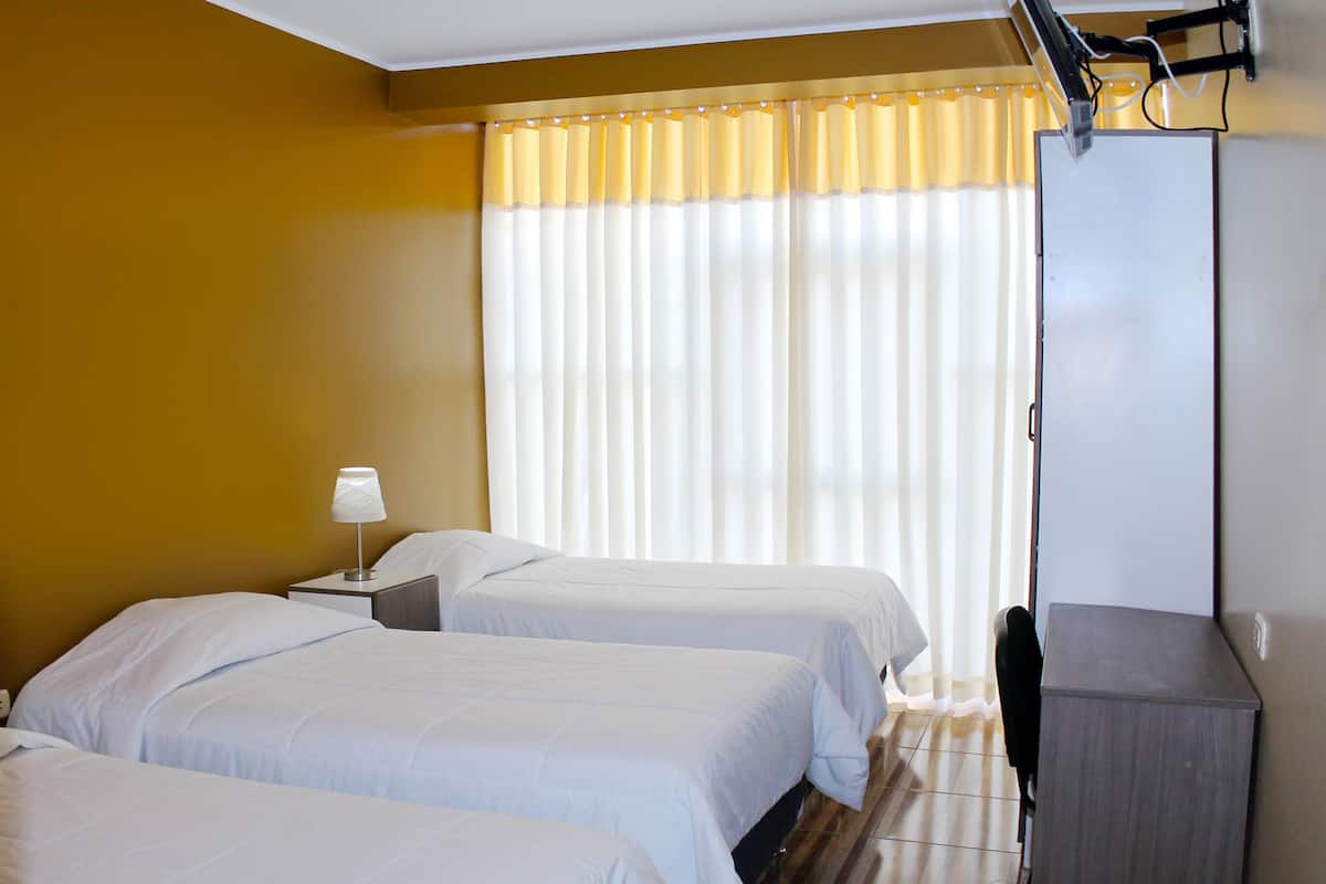 Quarto de hotel com duas camas, uma escrivaninha, uma lâmpada e uma TV fixada na parede.
