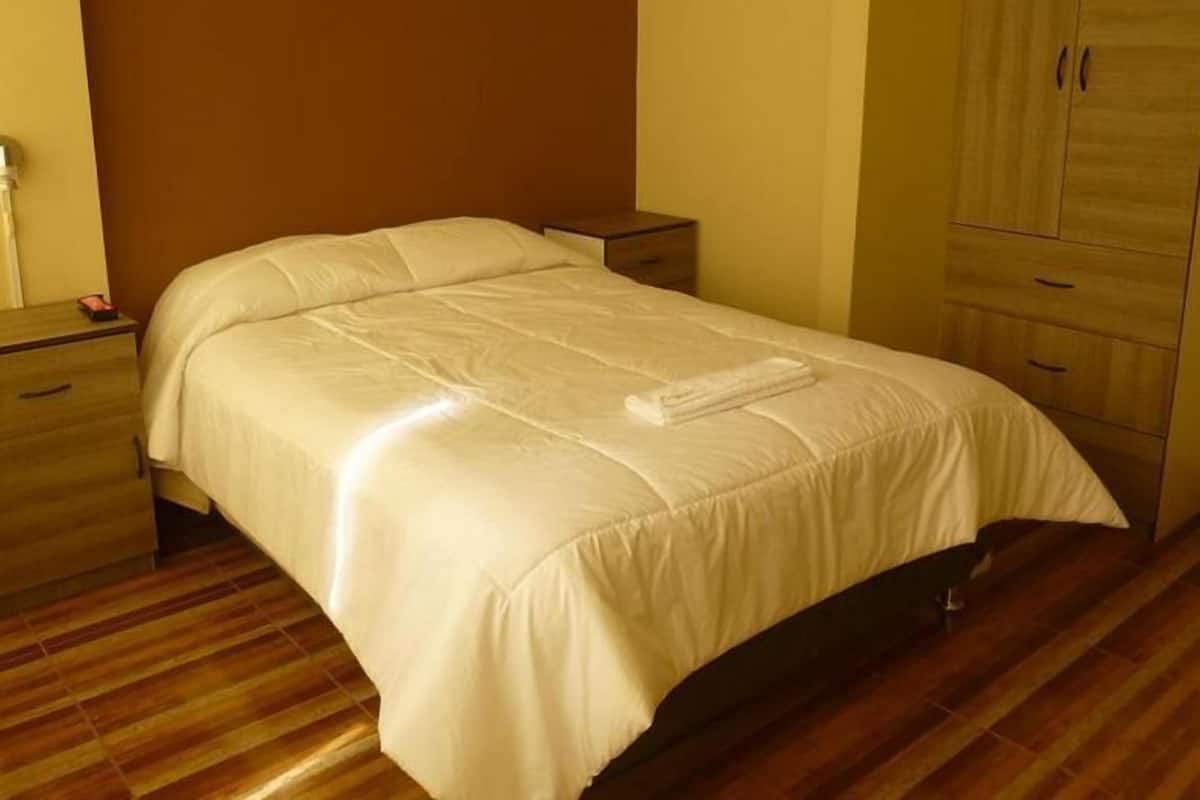 Cama bem arrumada em quarto com piso de madeira e armário.