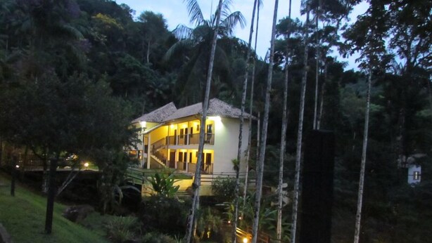 A two-story building with a balcony, surrounded by lush greenery and palm trees. - Pousada 3 Bacias (Resende)