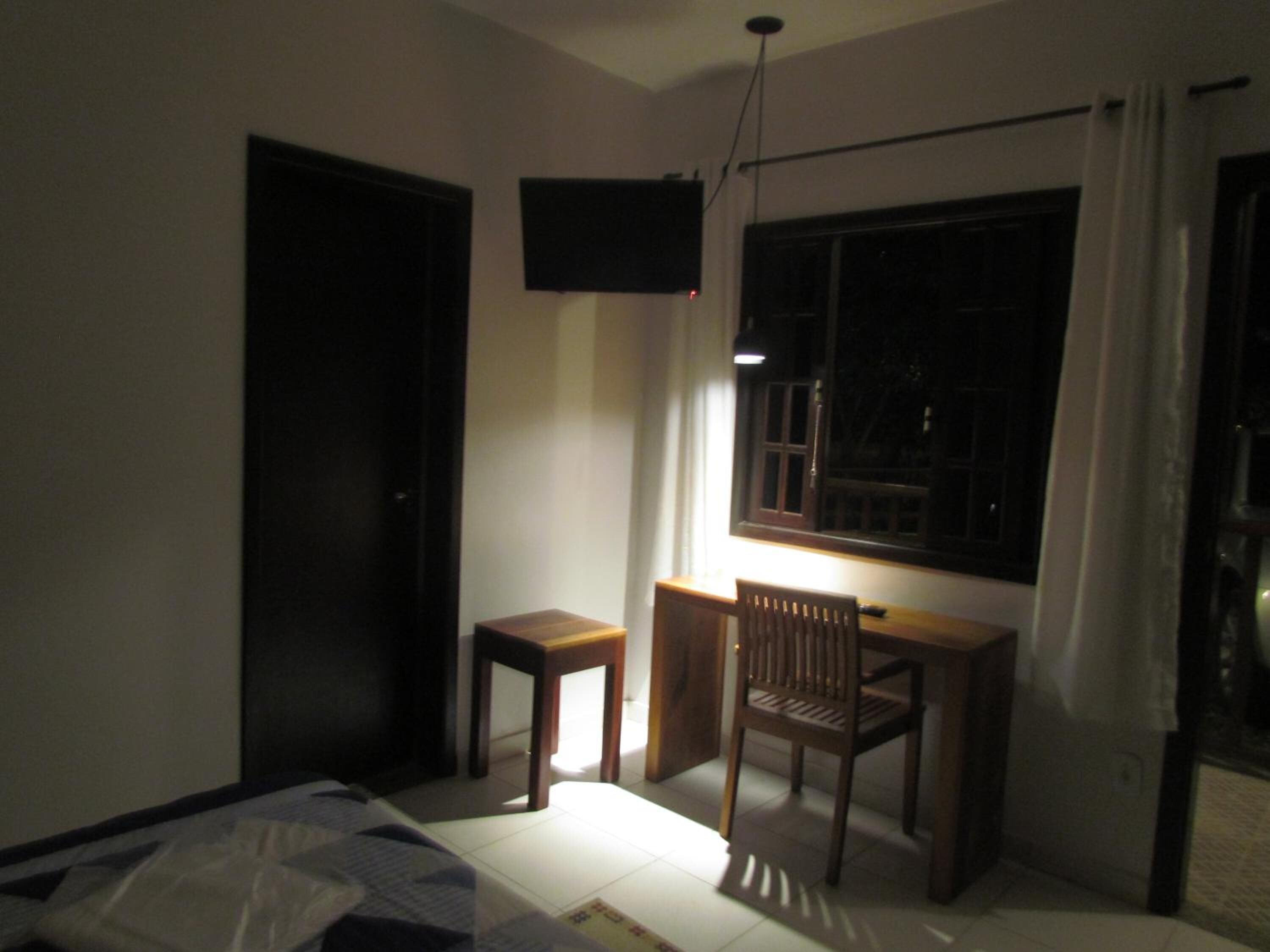 A small room with a bed, a desk, and a chair. There is a window with curtains and a TV mounted on the wall.
