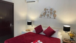 A hotel room with a bed, two bedside lamps, a wall-mounted air conditioner, and a decorative wall piece. - Pousada 3 Bacias (Resende)