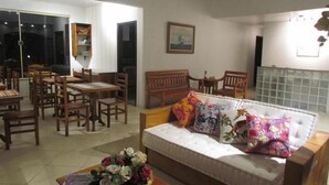 A living room with a sofa, wooden chairs, a dining table, and a flower arrangement. - Pousada 3 Bacias (Resende)