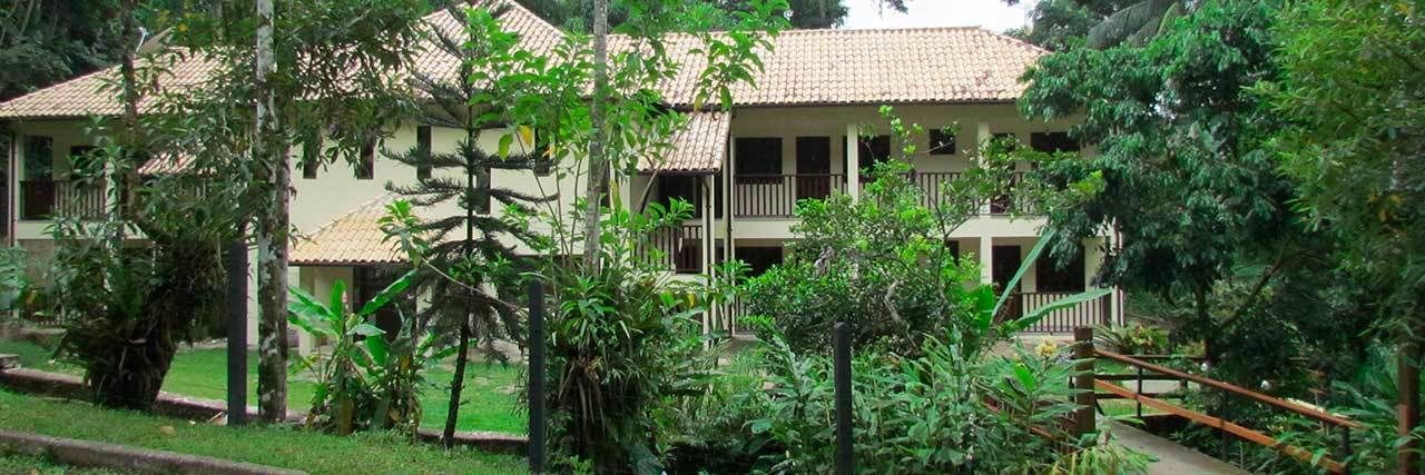 Um edifício de dois andares com telhado de telhas, cercado por vegetação exuberante.