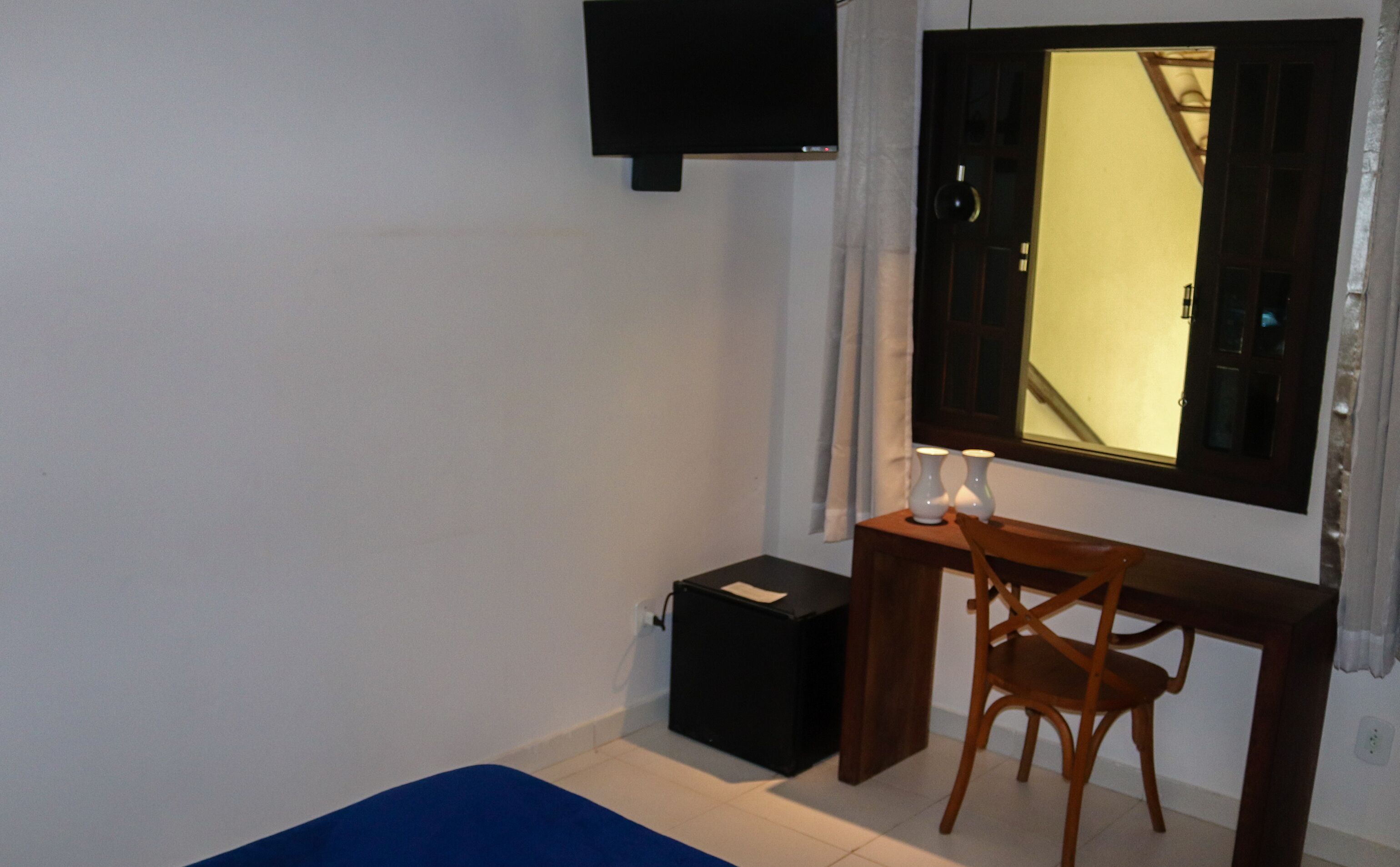A bedroom with a bed, a desk with a chair, a TV mounted on the wall, and a window with curtains.