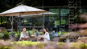 An outdoor dining area with a table and chairs, a large umbrella, and a glass wall with reflections of greenery. - Xiandai Gloria Grand Hotel Changsha (Changsha)