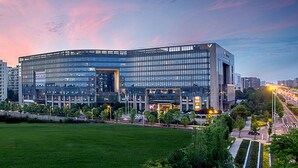 A modern building with a glass facade, surrounded by a well-maintained lawn and a road with vehicles. - Xiandai Gloria Grand Hotel Changsha (Changsha)