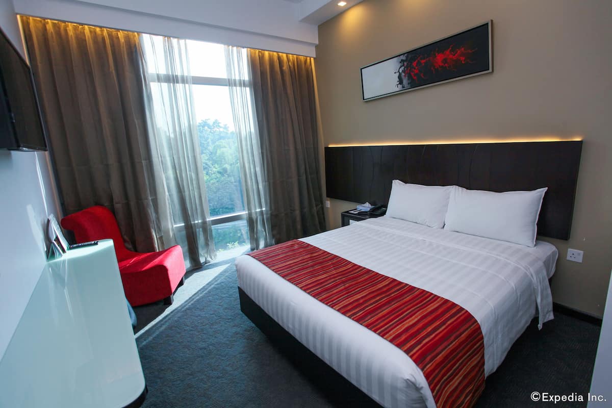Una habitació d'hotel amb un llit gran, una cadira vermella, un escriptori i una finestra amb cortines.