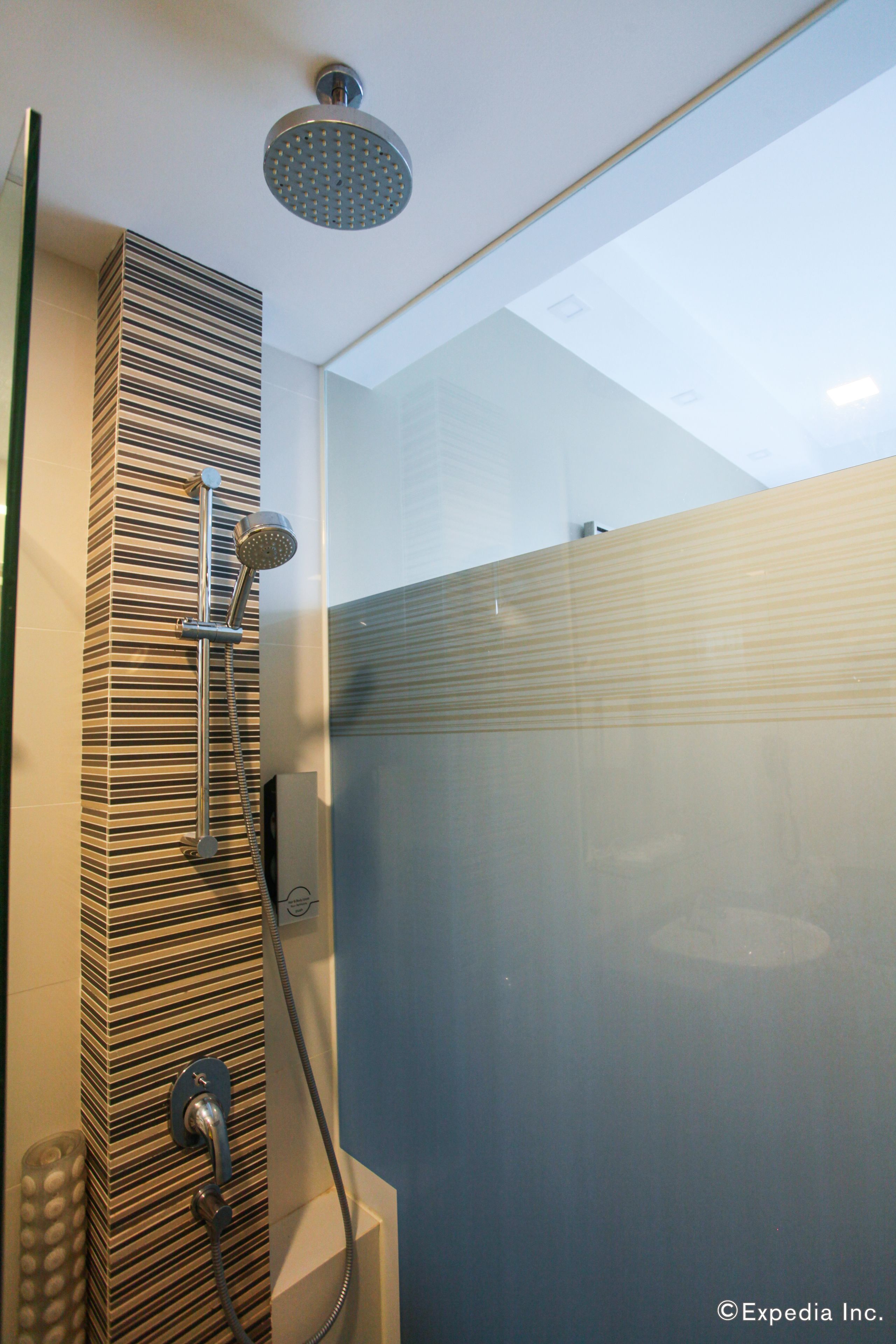 A modern shower with a rain showerhead and a handheld showerhead, a glass door, and a striped wall design.