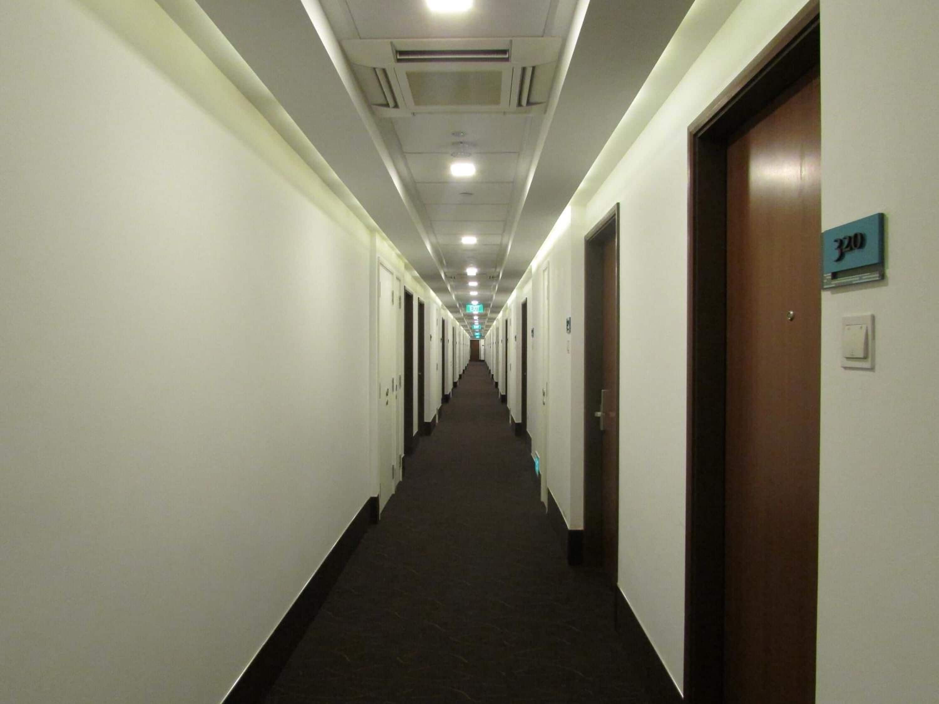 Un largo y estrecho pasillo de hotel con puertas a ambos lados, suelo alfombrado y un cartel que indica la habitación número 320.