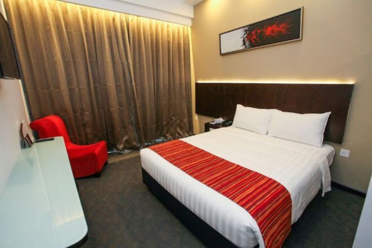 Una habitación de hotel con una cama grande, un escritorio, una silla roja y una cortina.