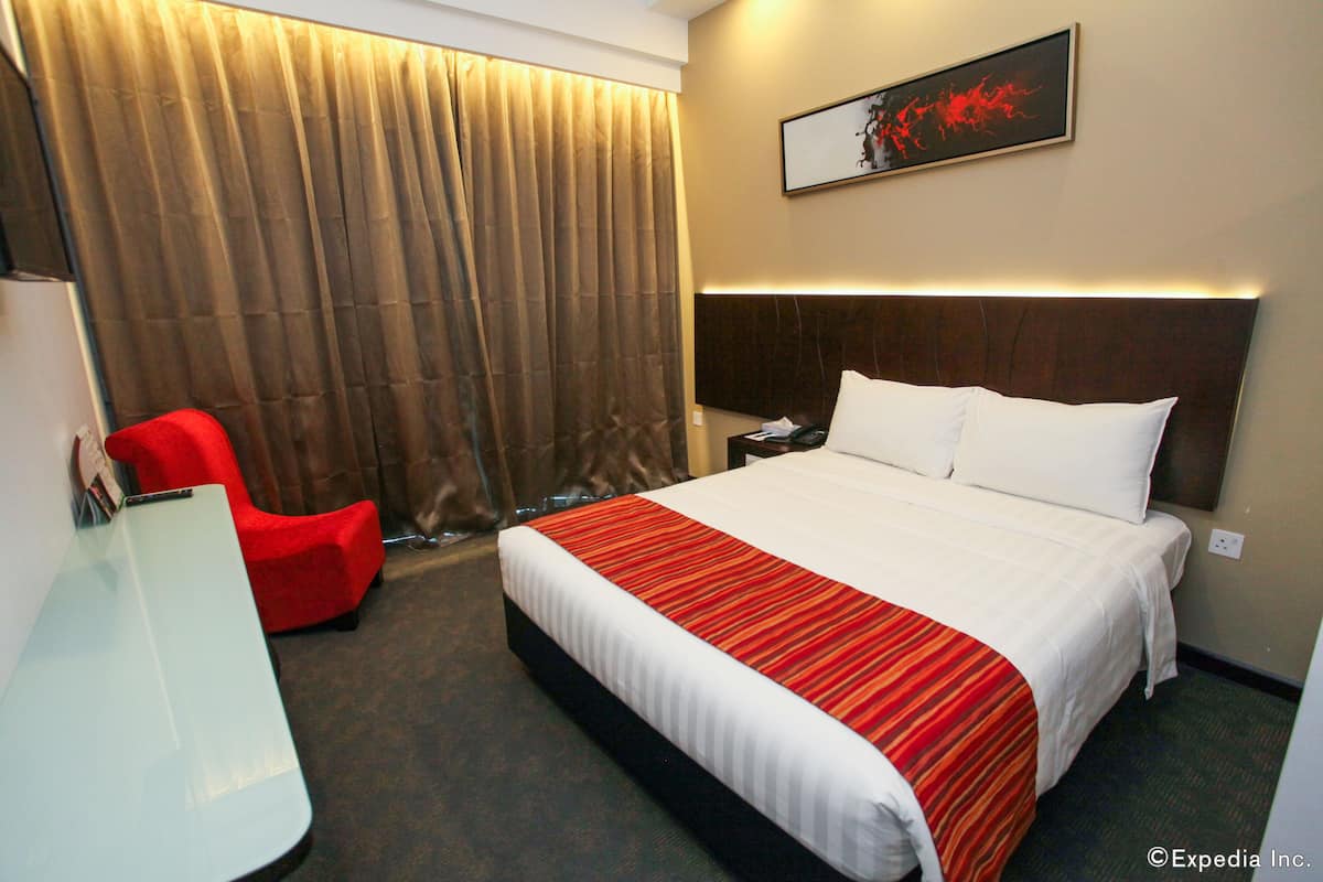 Habitació d'hotel amb un llit gran, un escriptori, una cadira vermella i una finestra amb cortines.