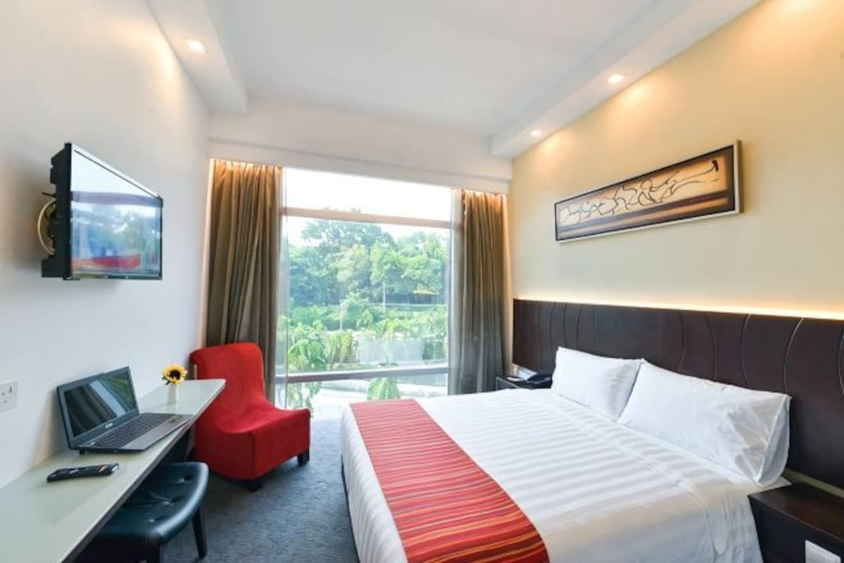 Una habitación de hotel con cama, escritorio, silla, televisión y ventana con cortinas.