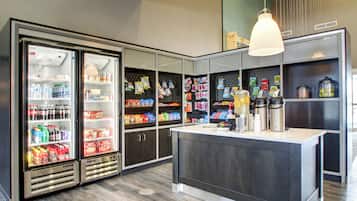 Ett modernt kök med två kylskåp fyllda med drycker, en köksö med en diskho och olika sorters förpackade snacks och kryddor på hyllorna.