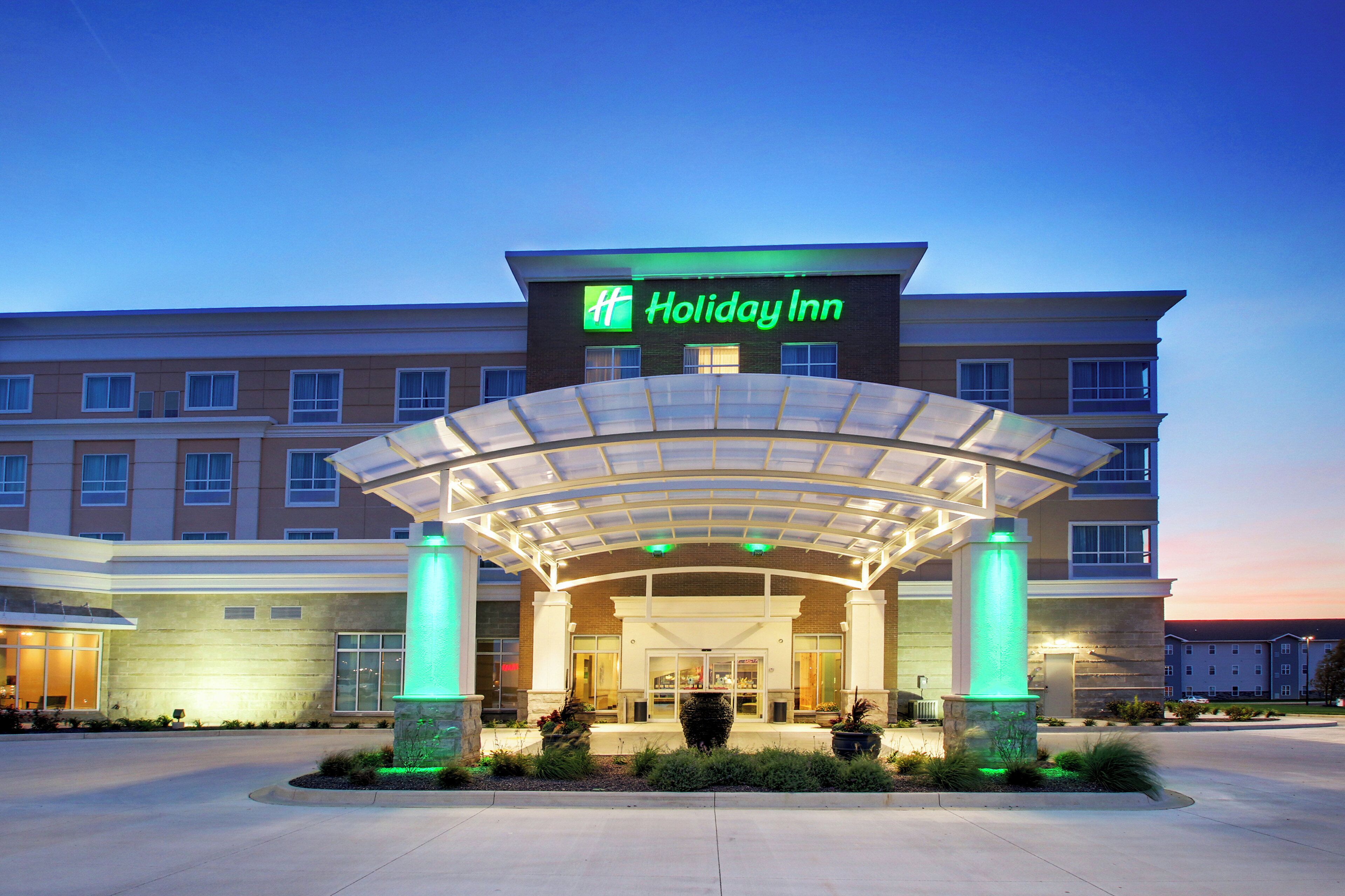Un hôtel Holiday Inn doté d’une entrée couverte, de plusieurs étages et d’un espace paysager agrémenté de plantes.