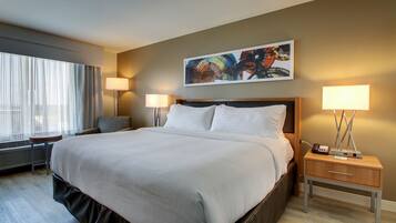 A hotel room with a large bed, two bedside tables with lamps, a window with curtains, and a painting on the wall.