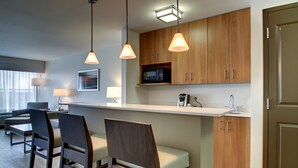 Una cocina moderna con armarios de madera, un microondas y luces colgantes. Hay sillas y una mesa en la zona de comedor.