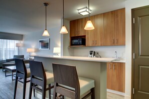A modern kitchen with wooden cabinets, a microwave, and pendant lights. There are chairs and a table in the dining area. - Holiday Inn & Suites Peoria At Grand Prairie by IHG (Peoria)
