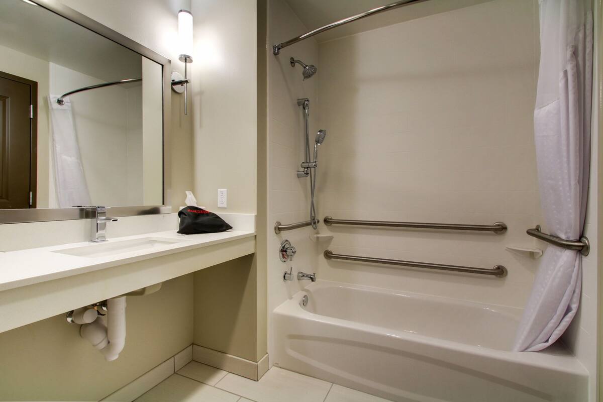 A modern bathroom with a white sink, mirror, and bathtub. There are grab bars installed for safety.